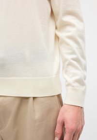 Pull beige clair en maille douce. Il présente un poignet et un ourlet côtelés, avec une texture lisse et un léger effet dégradé vers le bas.
