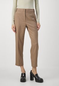 Pantaloni marroni a quadri con vestibilità su misura, vita media e lunghezza cropped. Indossati con scarpe platform nere lucide. Tessuto con texture liscia.