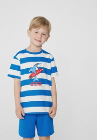 T-shirt rayé bleu et blanc avec un graphique de requin et du texte, associé à un short bleu uni. Fabriqué en matériau doux et respirant.