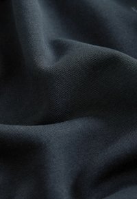 Tela de algodón de un azul marino oscuro que muestra una textura suave con un patrón de tejido visible, drapeada para revelar pliegues suaves y fluidos.
