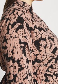 Kukallinen mekko, jossa on korkea kaulus, musta kangas, jossa on vaaleanpunaisia lehväkuvioita, sekä kokoontuva vyötäröyksityiskohta, joka antaa rakenteellisen siluetin.