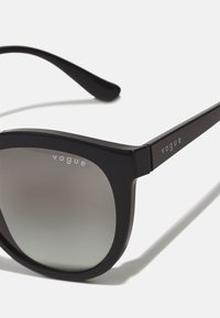 Ochelari de soare negri cu ramă rectangulară, având lentile gradient. Brațele au gravat în argint „vogue”. Textură netedă, design modern.