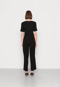 Czarny prążkowany kombinezon z krótkimi rękawami, dopasowanym topem, szerokimi nogawkami i ściągniętą talią, noszony z czarnymi butami na obcasie.