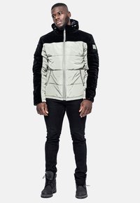 Vadderad jacka i ljusgrå med svarta sammetsärmar, dragkedja fram, fast huva och två sidofickor. Buren med svarta tajta jeans och stövlar.