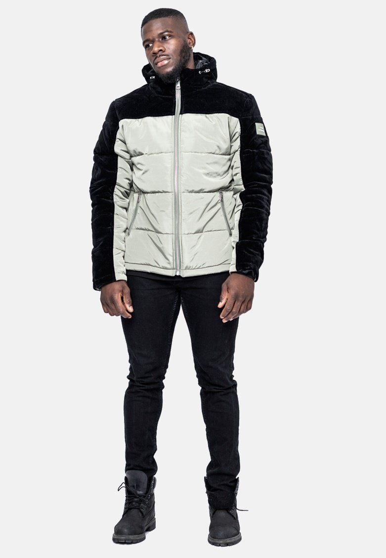 Vadderad jacka i ljusgrå med svarta sammetsärmar, dragkedja fram, fast huva och två sidofickor. Buren med svarta tajta jeans och stövlar.