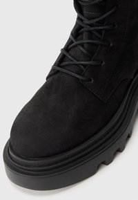 Stivale alla caviglia in suede nero con punta tonda, suola resistente in gomma nera e dettagli testurizzati a contrasto lungo i lati e i lacci.