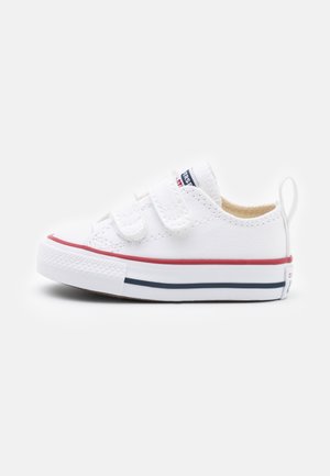 White canvas sneaker with dual hook-and-loop straps, red and navy stripe accents, rubber toe cap, and textured sole.