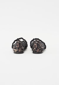 Chaussures plates avec un motif léopard noir et marron, un dessus texturé avec des perforations décoratives, et un dos élastique flexible.