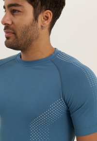 Blue athletic shirt featuring a smooth texture, short sleeves, and dotted pattern along the shoulders, with a round neckline and fitted design.