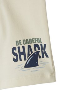 Text "Be careful shark" printed on beige fabric with a dark blue shark fin rising from light blue water waves.