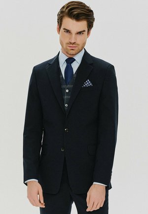 Granatowa marynarka w stylu slim fit z klapami o wycięciu, z jednym guzikiem i kieszenią na piersi z poszetką w kropki. Spodnie z płaskim przodem.