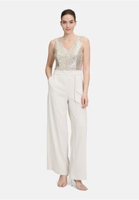 Złota tank top z cekinami, połączona z szerokimi spodniami w kolorze kremowym z detalem kieszeni. Przezroczyste sandały na obcasie dopełniają stylizację.