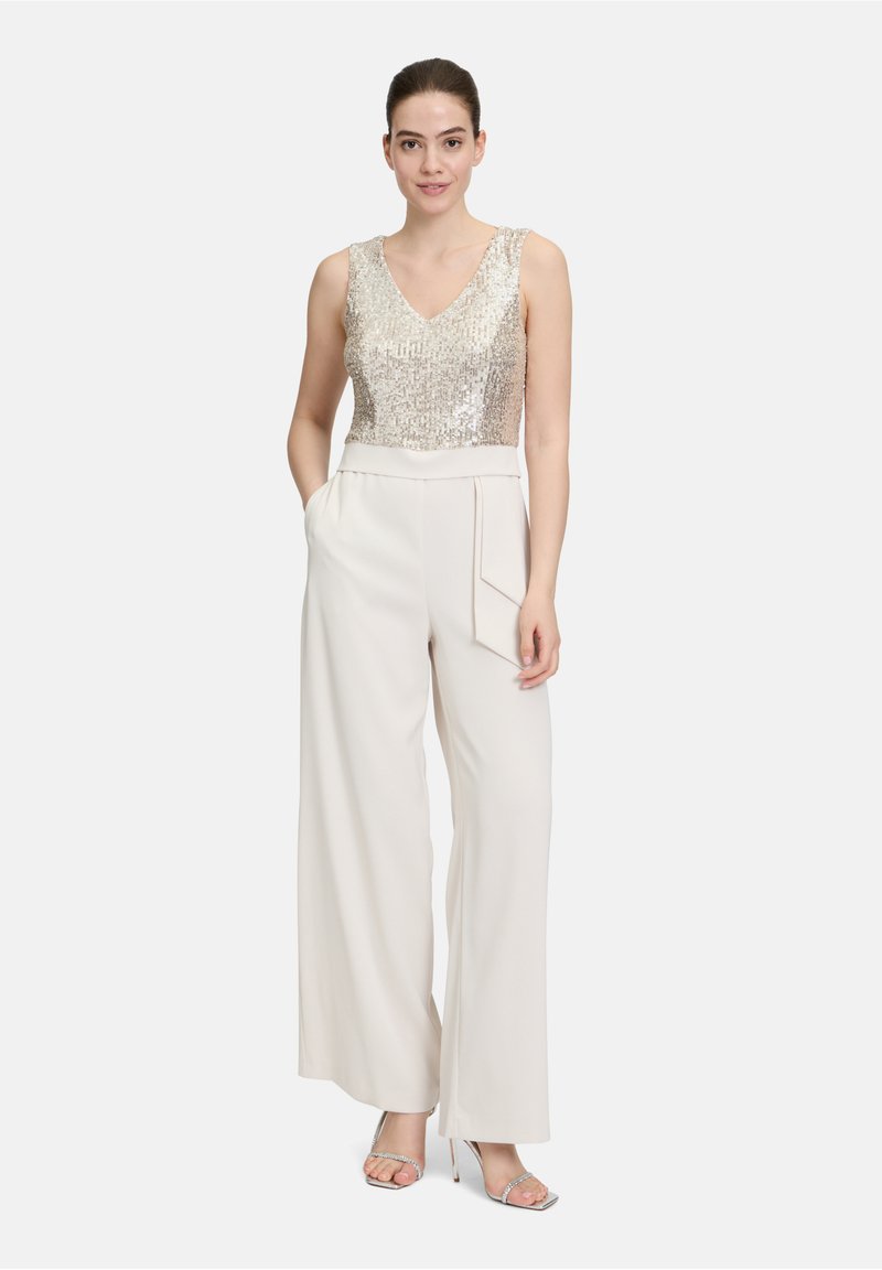 Złota tank top z cekinami, połączona z szerokimi spodniami w kolorze kremowym z detalem kieszeni. Przezroczyste sandały na obcasie dopełniają stylizację.