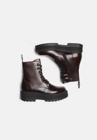 Bottines en cuir bordeaux avec semelle en caoutchouc noir, avec un lacet à l'avant, une fermeture éclair sur le côté et une languette pour un enfilage facile.