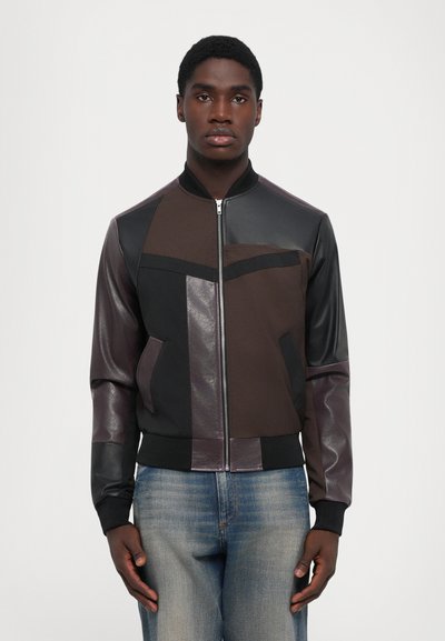 Braune und schwarze Bomberjacke mit Leder- und Stoffelementen, geripptem Kragen und Bündchen, mit einem Reißverschluss vorne und zwei Seitentaschen.