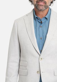 Blazer gris claro con una tela texturizada, diseño de un solo botón, dos bolsillos delanteros y botones de color claro sobre una camisa a cuadros azul.
