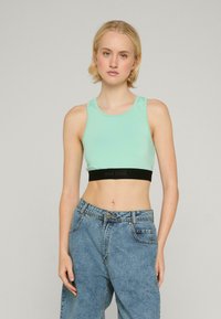 Minton grøn, cropped tanktop med et sort elastikbånd med tekst. Glat, strækbart stof, rund halsudskæring og ærmeløs design.