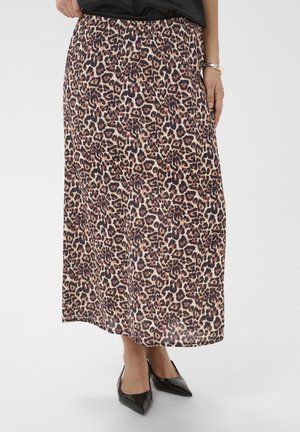 Femme portant une jupe mi-longue à imprimé léopard, des talons noirs à bout pointu et un haut noir, avec un bracelet argenté au poignet.