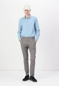 Chemise bleu clair à manches longues, pantalon gris ajusté, chaussures noires et casquette beige. Tenue décontractée avec un design simple et des couleurs neutres.