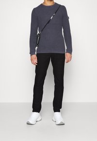 Granatowy sweter dziergany o fakturowanej powierzchni, w połączeniu z czarnymi spodniami w kratę oraz białymi sneakersami z masywną podeszwą. Czarna torebka na ramię.