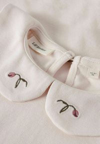 Helles rosa Baumwolloberteil mit rundem Kragen. Auf beiden Seiten mit gestickten rosa Blumen und grünem Stiel verziert. Versteckter Druckverschluss auf der Rückseite.