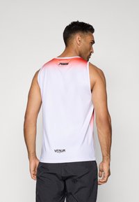Débardeur de sport pour homme en blanc avec des accents en dégradé rouge. Présente un design sans manches, un logo à l'arrière et une texture de tissu respirant.