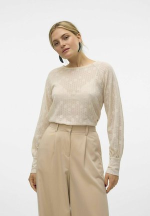Haut à manches longues texturé beige avec un motif floral subtil, associé à un pantalon taille haute beige avec des plis et une coupe décontractée.