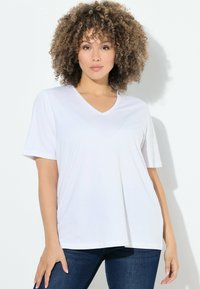 T-shirt bianca a V con maniche corte, realizzata in un tessuto morbido. Vestibilità casual con una superficie liscia, abbinata a jeans blu scuro.