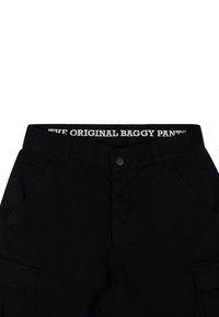 Melni brīvie bikses ar augstu jostu un baltu logo "ORIGINAL BAGGY PANTS". Iespējas sānu kabatas un pogu priekšpusē.