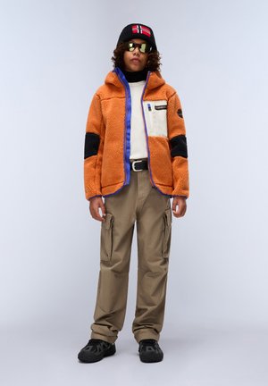 Orange fleece jacket with blue and black accents, cream chest pocket; beige cargo pants; black sneakers; black beanie with flag detail; sunglasses.