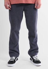 Pantalon en velours côtelé gris avec une texture côtelée verticale, coupe droite, associé à des baskets noires avec des lacets blancs et des bandes latérales.