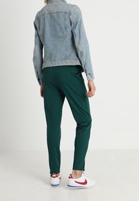 Jasnoniebieska kurtka dżinsowa, zielone spodnie sportowe i białe sneakersy z czerwonymi akcentami. Gładkie tekstury i casualowy design odpowiednie do aktywnego stylu życia.