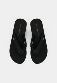 Μαύρα σαγιονάρες με πλεγμένους ιμάντες, ματ πέλμα και χρυσή λεπτομέρεια λογότυπου. Απλός, επίπεδος σχεδιασμός κατάλληλος για καθημερινή χρήση.