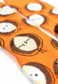 Calze di cotone arancioni con un motivo ripetuto di volti di cartoni animati contornati di marrone, con occhi bianchi e espressioni varie.