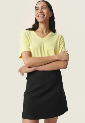 Gul V-hals T-shirt med korte ærmer parret med en sort mini-nederdel. Glat, letvægtigt stof med et enkelt design og afslappet pasform.
