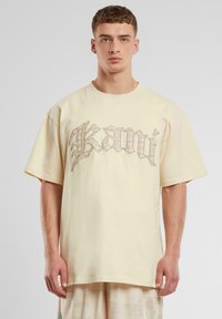 Yellow cotton t-shirt with a loose fit, round neck, and short sleeves. Features a decorative silver graphic text design on the front.