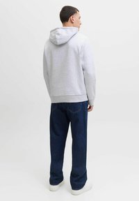 Sudadera con capucha de color gris claro, con un ajuste ceñido, que cuenta con cordones, puños acanalados y un dobladillo recto, combinada con unos vaqueros oscuros sueltos.