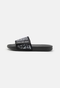 Černé sandály s plochou podrážkou s měkkým páskem a bílým logem Calvin Klein Jeans a opakovaným designem textu na strukturované podrážce.