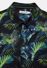 Krátký rukáv košile z černé tkaniny se živým vzorem palmových listů v zelené a modré barvě; zahrnuje límec a zapínání na knoflíky.