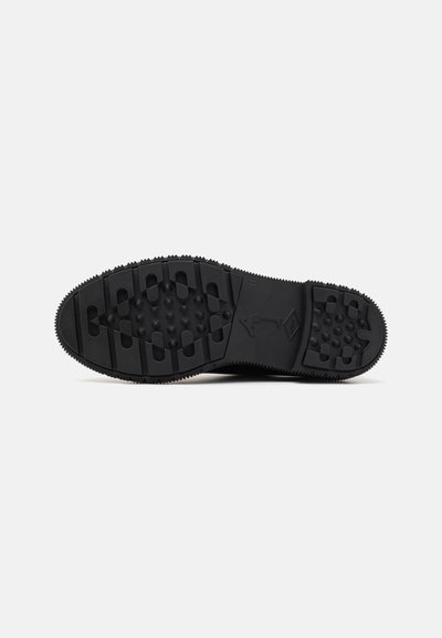 Black athletic shoe sole with a textured rubber surface, featuring multiple traction patterns and ridges for grip.
