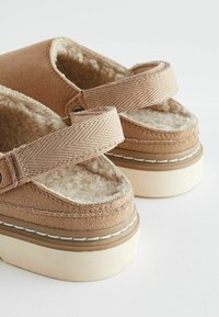 Beige platform slide sandals with a soft, furry interior, textured straps, and contrasting stitching on a cream-colored sole.