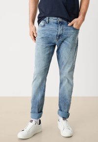 Jeans de mezclilla azul claro con un ajuste relajado, puños enrollados, diseño de cinco bolsillos y costuras en contraste, combinados con zapatillas blancas.