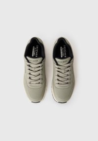 Et par lysegrå Skechers sneakers med perforerte tær, svart innvendig fôring og matchende snørebånd på hvit bakgrunn.