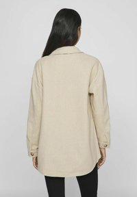 Giacca button-up oversize beige, realizzata in tessuto texturizzato, caratterizzata da un taglio dritto, grande colletto e polsini con bottoni.
