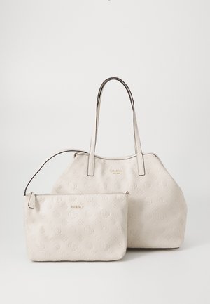 Beżowa teksturowana torba typu tote Guess z długimi uchwytami i dopasowanym paskiem zapinanym na zamek, obie z tłoczonymi logo i wzorem monogramu.