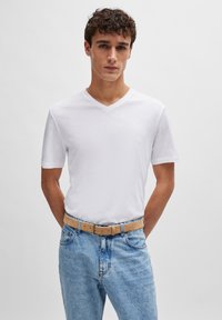 Valkoinen V-kaula-aukkoinen T-paita, joka on valmistettu kevyestä kankaasta, yhdistettynä vaaleansiniset farkut ja kermaisen värinen vyö. Yksinkertainen muotoilu, neutraalit värit.