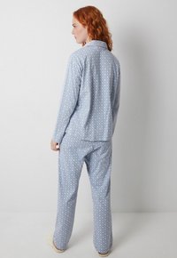 Lyseblå pyjamas sæt med diamantmønster, lange ærmer og løstsiddende bukser. Materialet ser blødt og behageligt ud.
