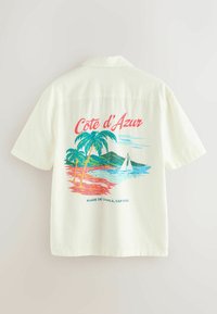 Chemise blanche à manches courtes avec une scène de plage colorée, des palmiers, un voilier et le texte « Côte d'Azur, Plage de la Mala, Cap d'Ail » au dos.