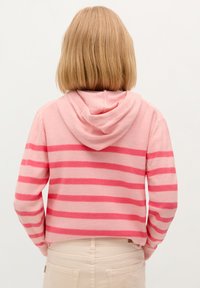 Haut à capuche rose clair avec des rayures horizontales rose foncé. Il a une capuche et une coupe raccourcie, fabriqué en tissu doux avec une texture lisse.