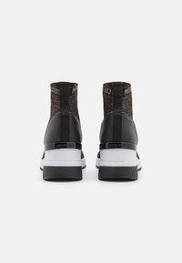 Baskets montantes noires en tissu texturé, avec un motif accentué et une semelle blanche contrastante. Présente un détail en plastique noir au niveau du talon.